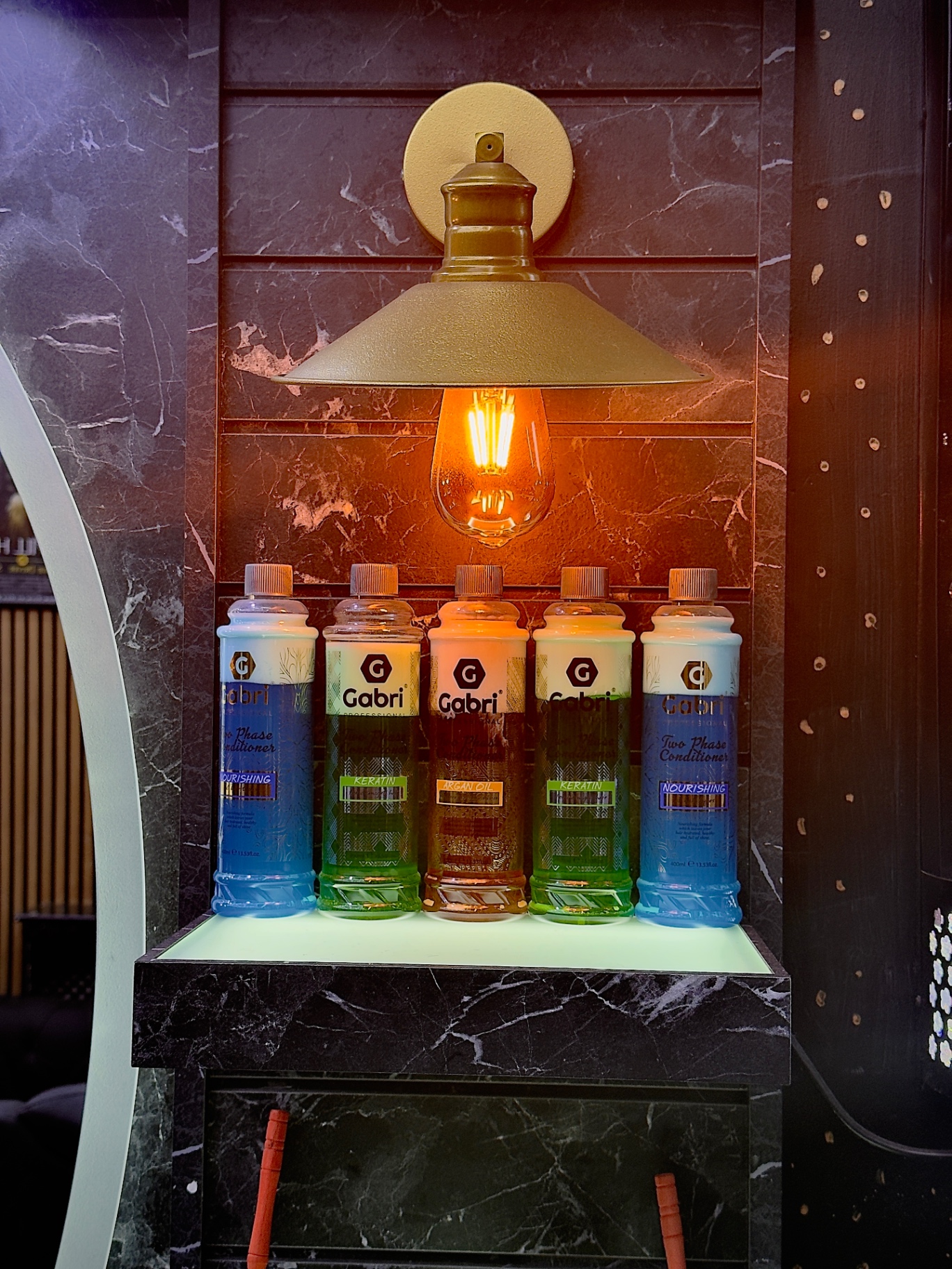 Shelf of professional hair conditioners lit by a warm brass lamp at Xalo Barbers